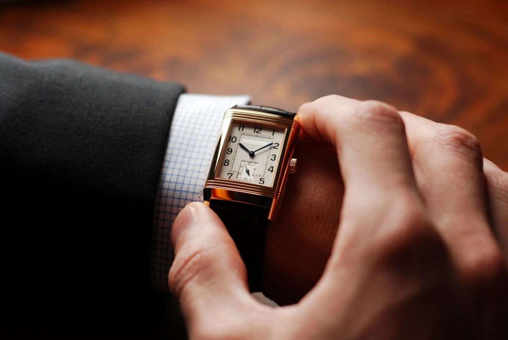 Close-up of a person adjusting a square wristwatch with a leather strap.