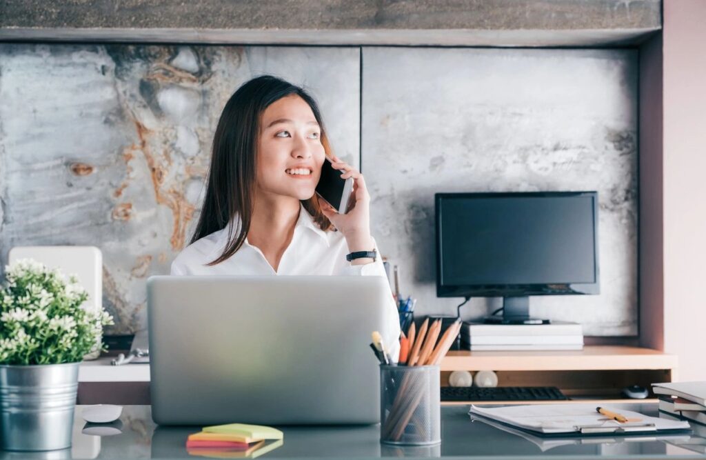 Woman on phone at desk with laptop.